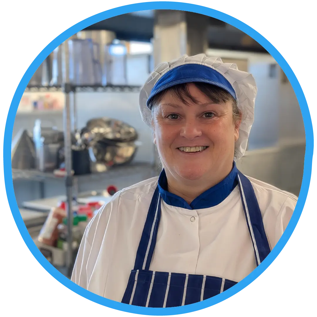 Denbighshire school chef in a school kitchen wearing her whites and a blue apron. The chef is smiling.